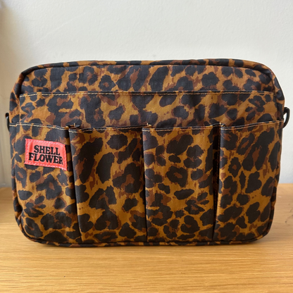 Leopard print bag with a visible brand label on a wooden surface.