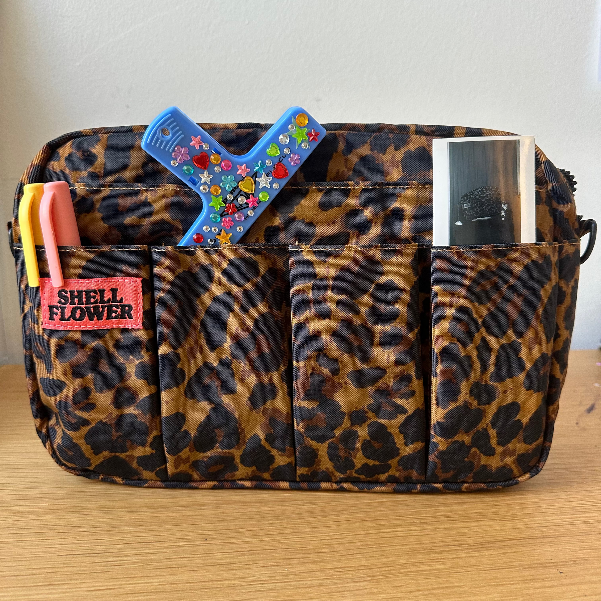 Leopard print bag with stationery items on a wooden surface