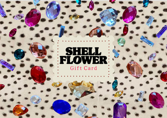 A Shell Flower gift card centered on a beige leopard-print background scattered with colorful faceted gemstones. The card reads 'SHELL FLOWER Gift Card' in black and pink text.
