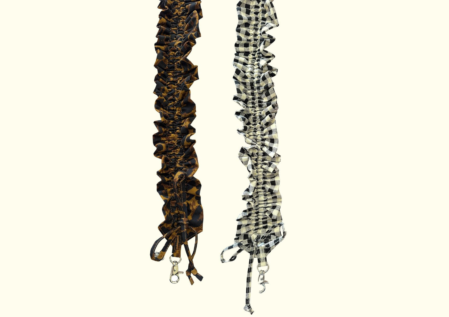 Two long ruffled fabric straps hanging vertically on a plain light beige background. The left strap is dark brown with a leopard-like pattern, and the right strap is black and white checkered.
