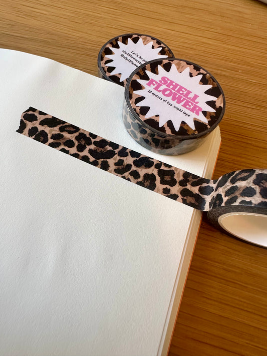 Leopard print washi tape with a visible brand name on a wooden surface.